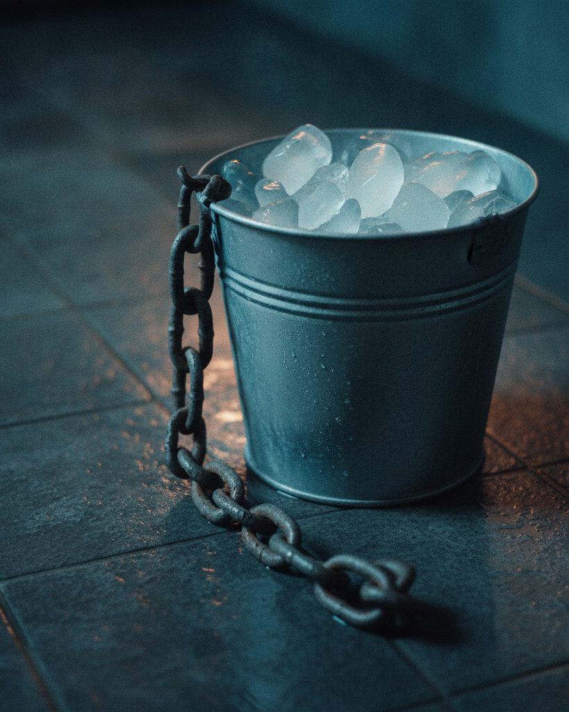 A galvanised bucket of cracked ice beside a heavy pull-chain on wet stone