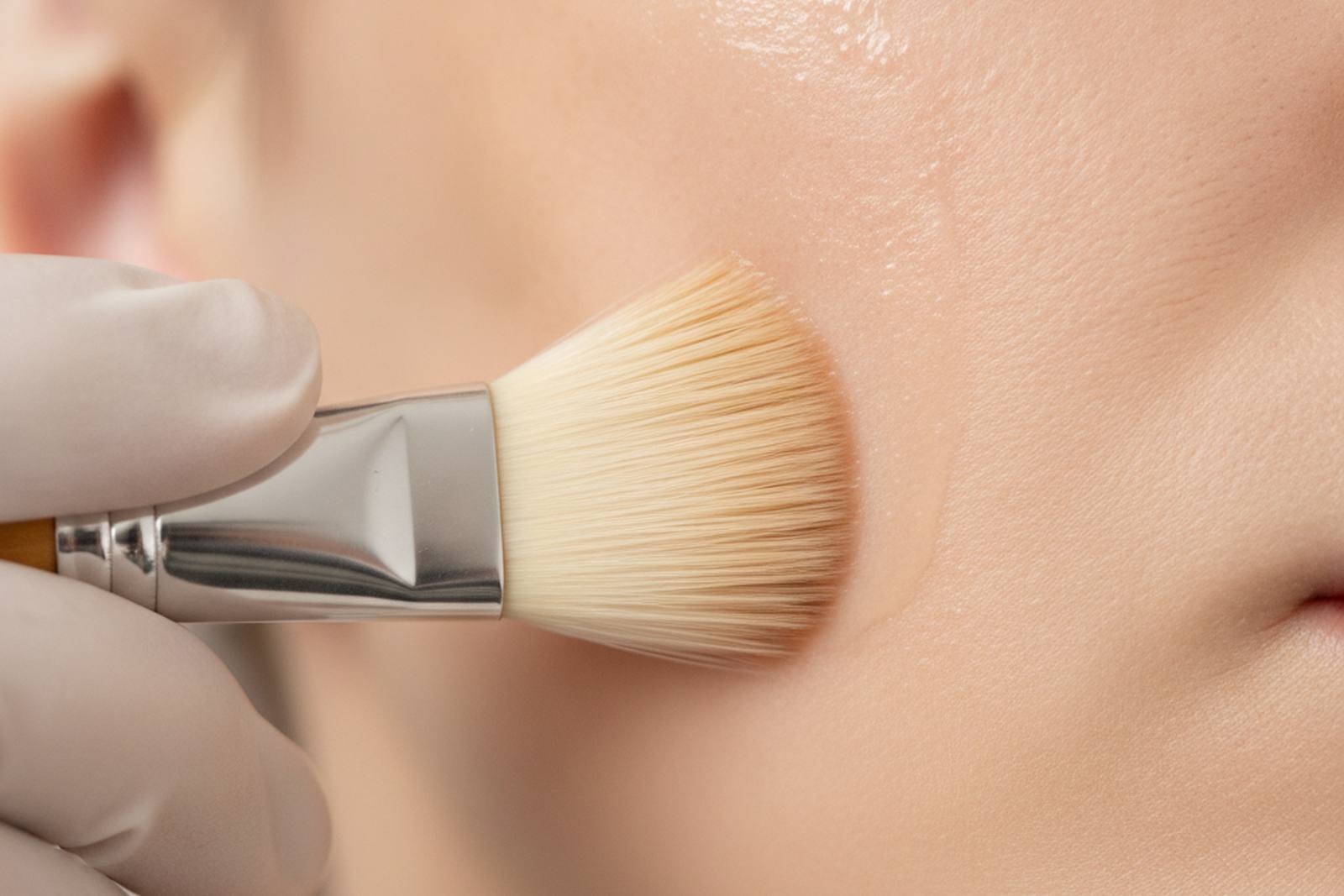 A soft brush applying serum to cheek skin