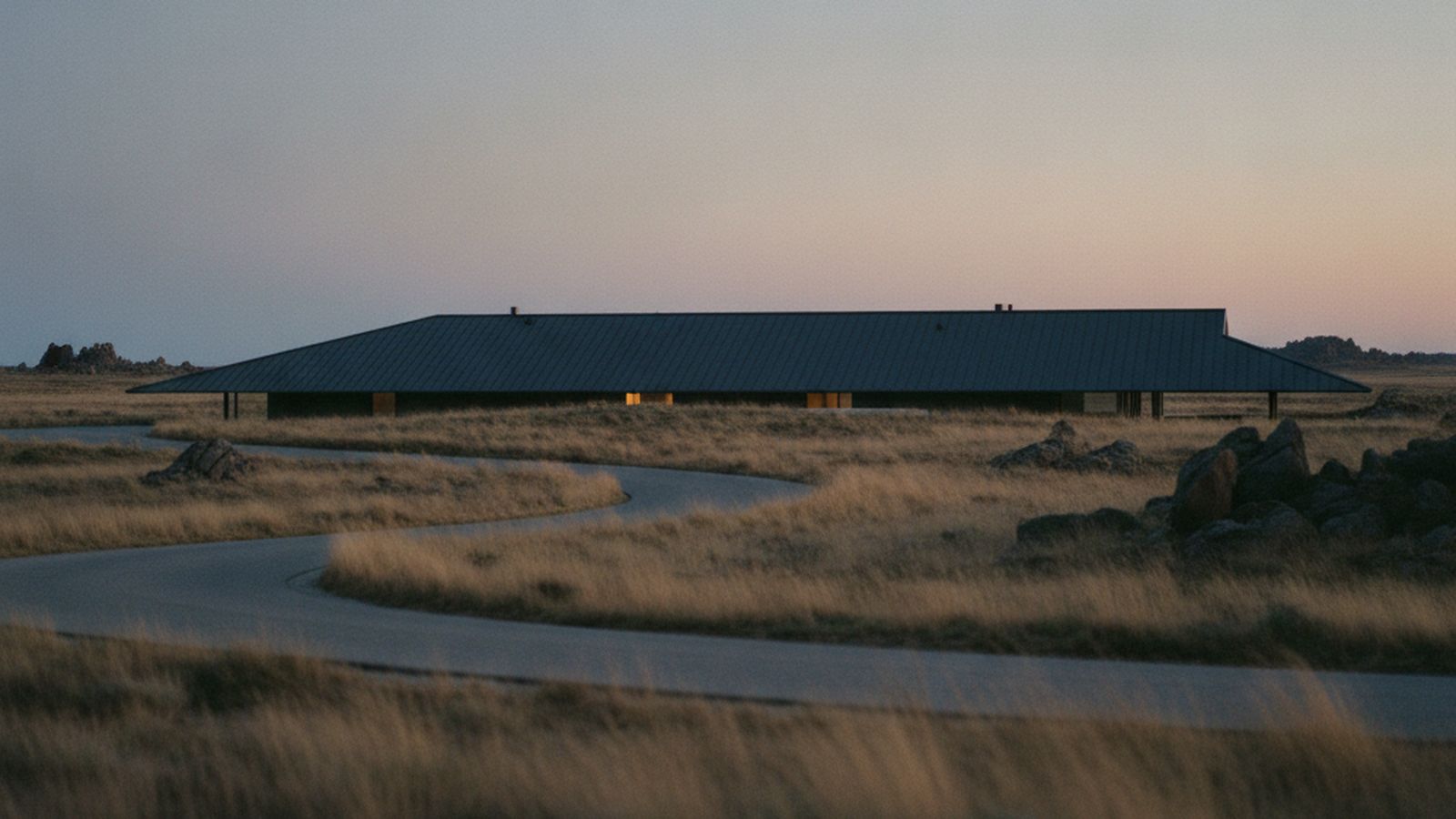 The single roof plane of Ridgeline House seen from the approach road, low horizon at dusk