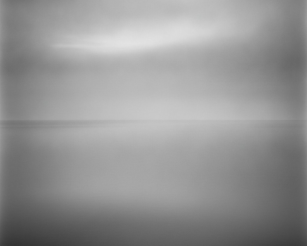 A calm, near-empty sea meeting a pale sky at a low, misty horizon