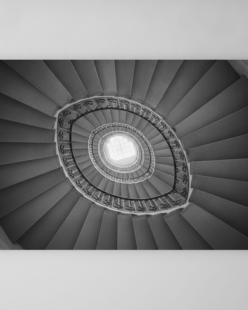 A spiral staircase seen from below, its steps coiling up to a bright square skylight
